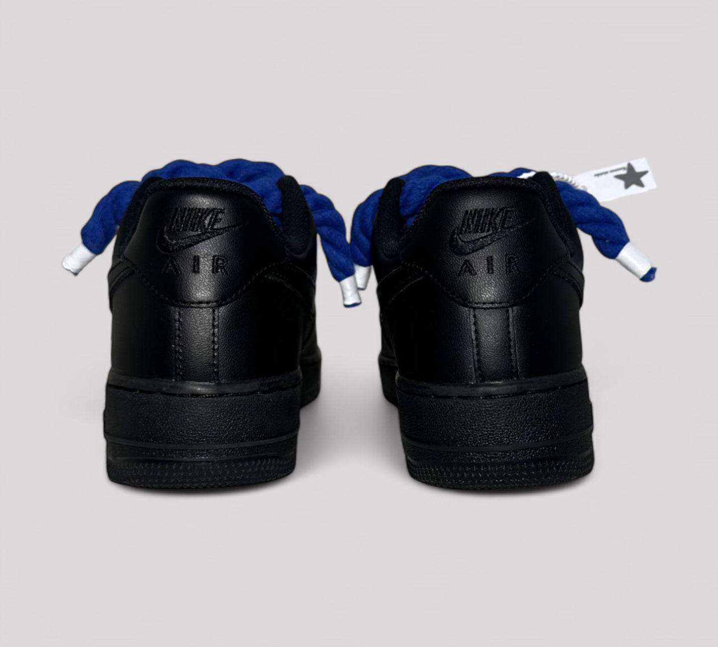 Black Nike Air Force sneakers with blue rope laces on a light gray background