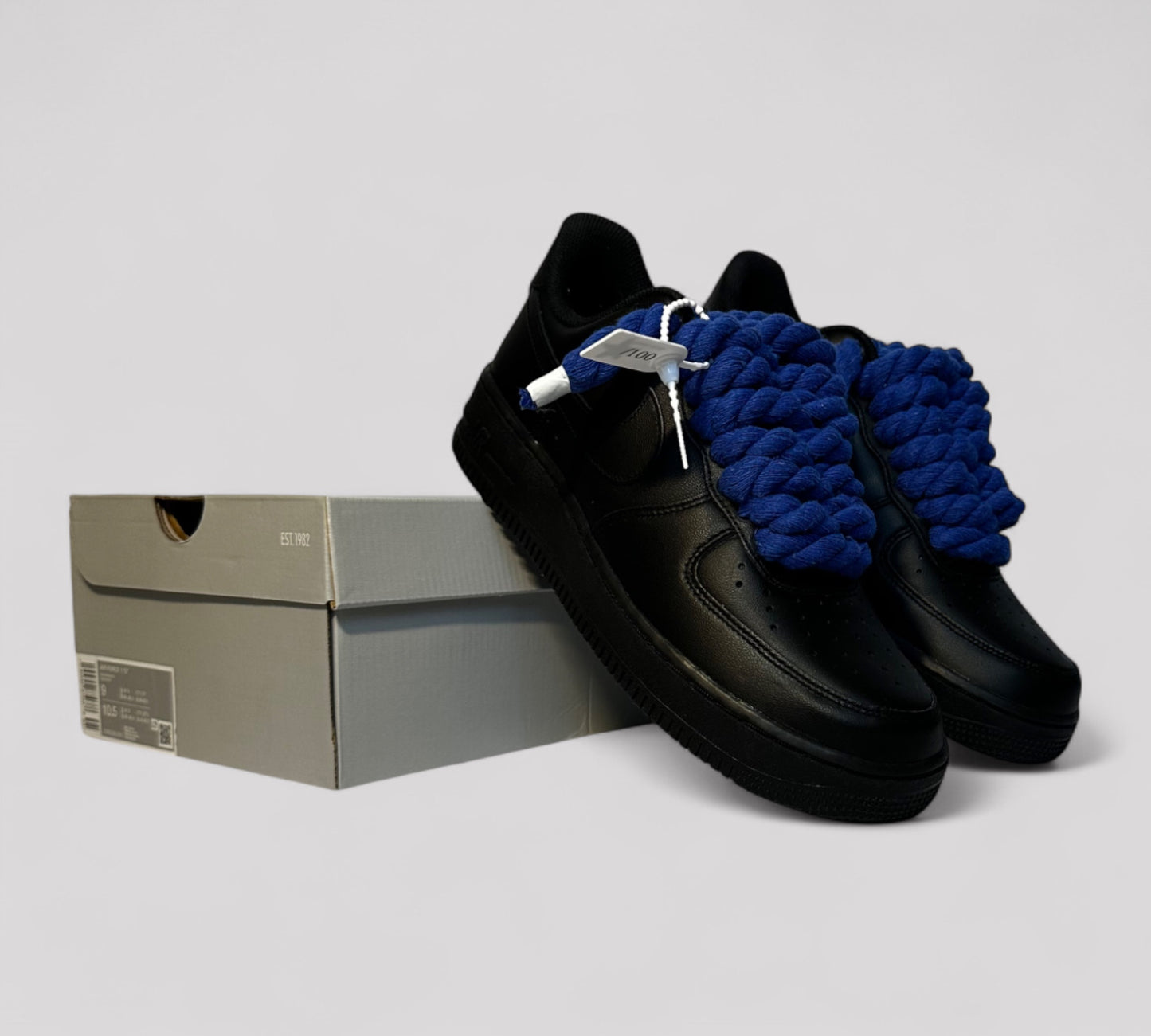 Black shoes with blue rope laces and a gray box on a light gray background