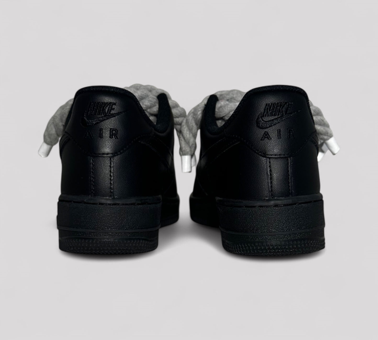 Black Nike Air Force sneakers shown from the back on a light gray background