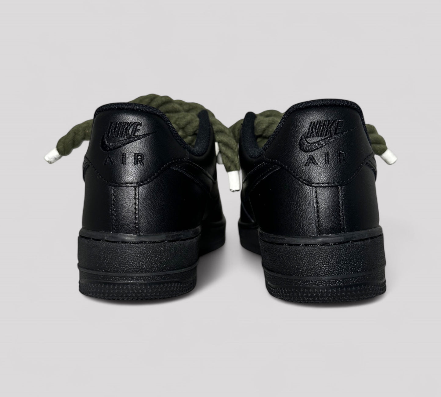 Black Nike Air shoes with khaki rope laces on a light gray background