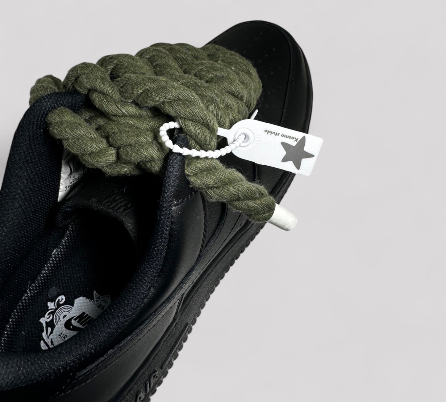 Black sneaker with green rope laces and a visible brand tag on a light gray background