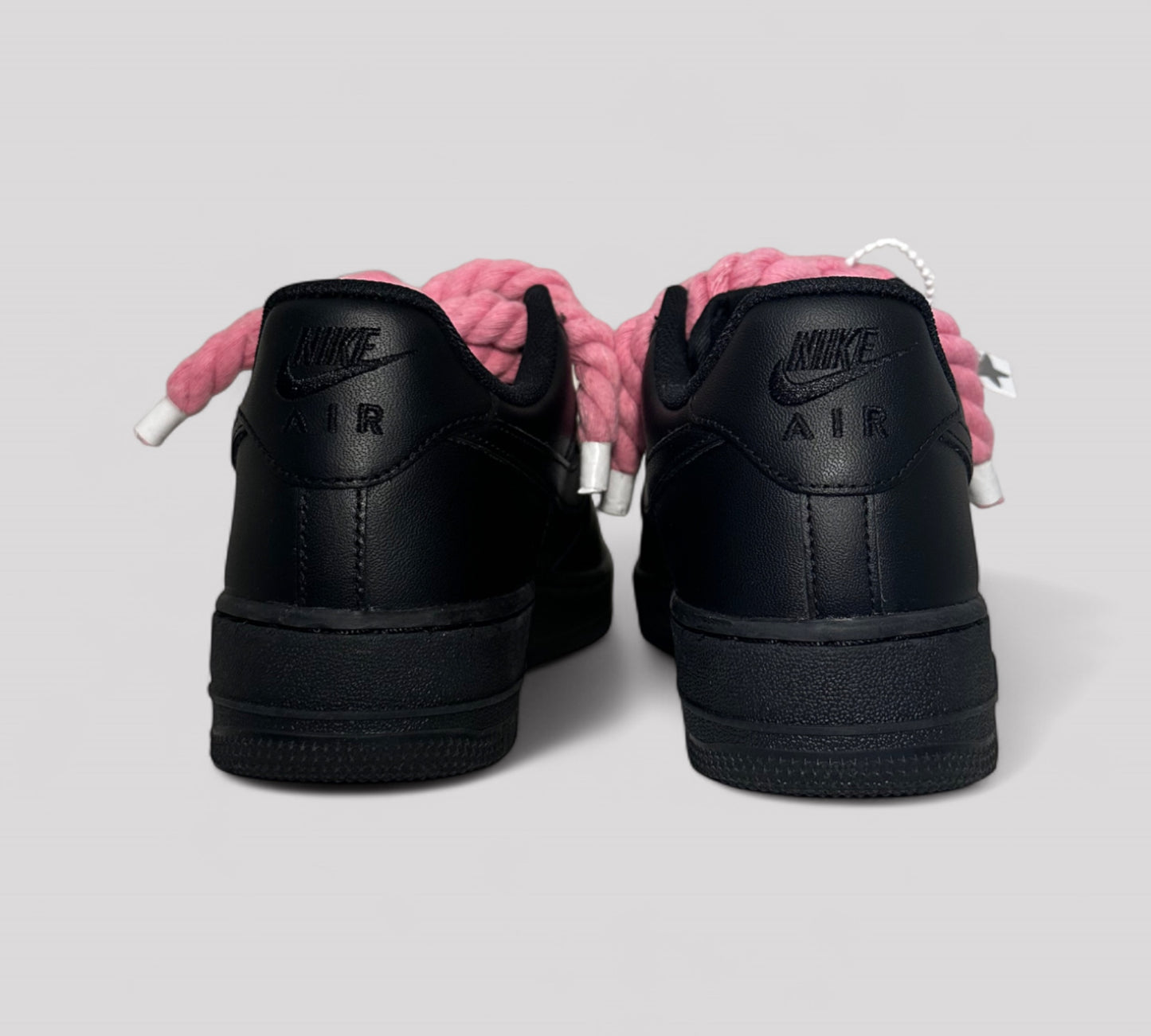 Black Nike Air Force sneakers with pink roep laces on a light gray background
