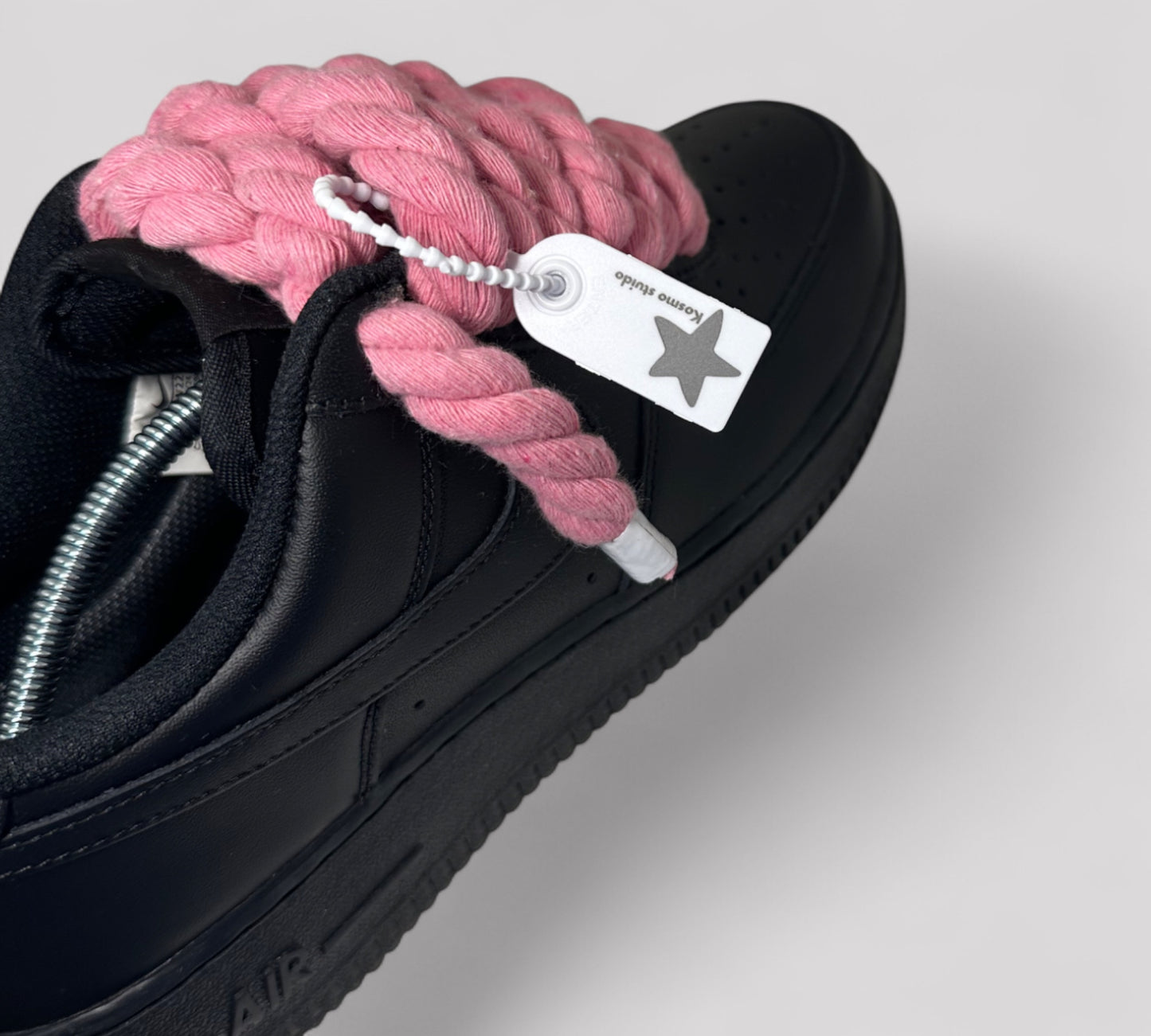 Black sneaker with pink rope laces and a visible brand tag on a light gray background