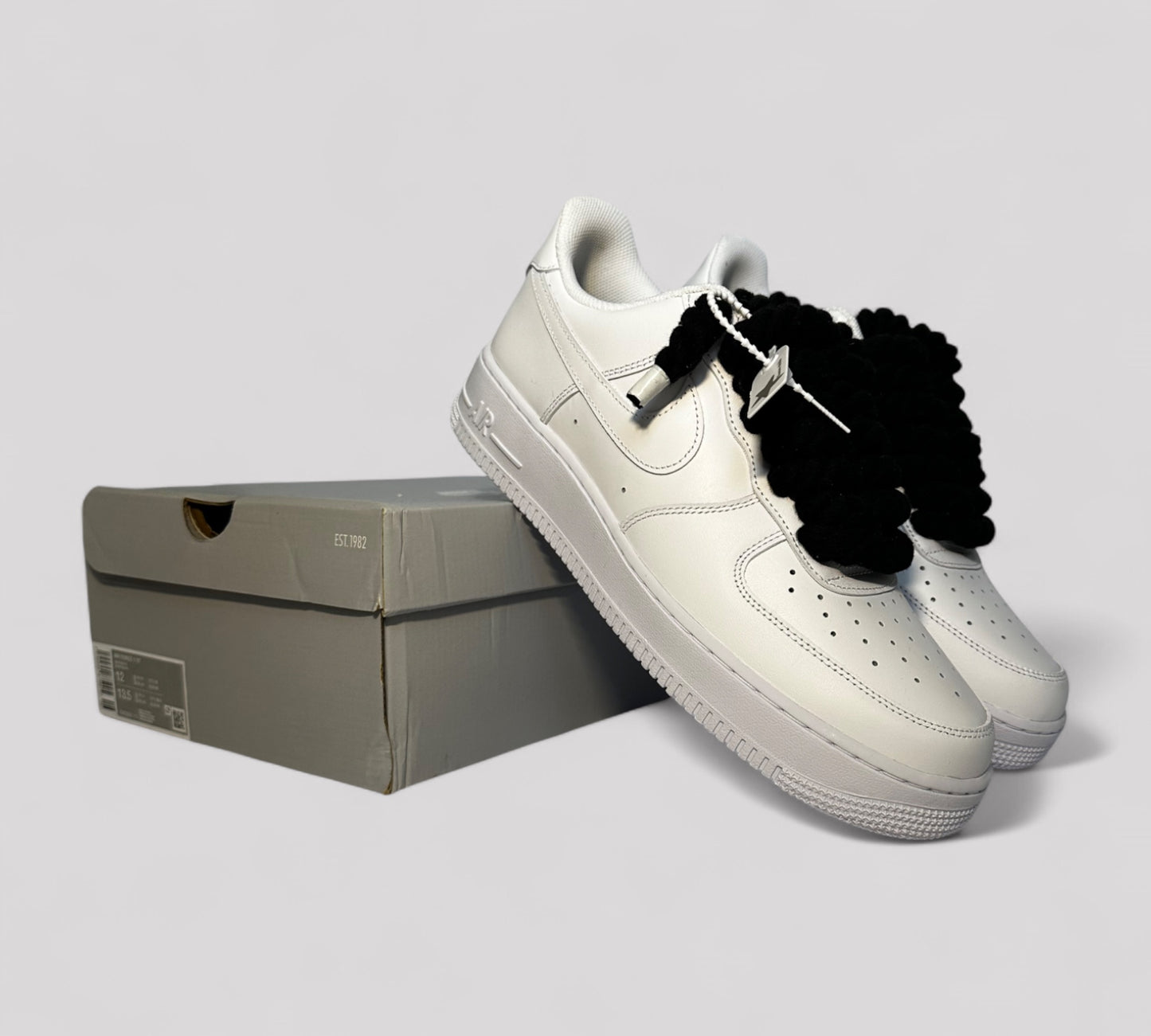 White Air force 1 with black rope laces on a light gray background