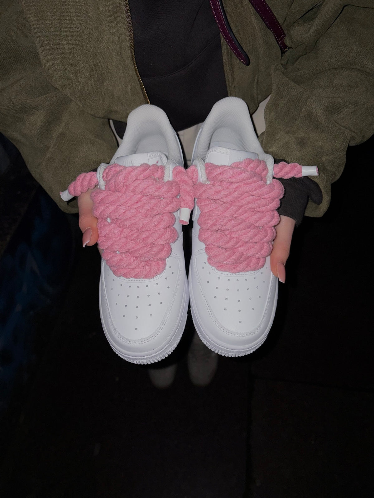 Ruce drží bílé Nike Air Force 1 s růžovými rope laces – Kosmo Studio