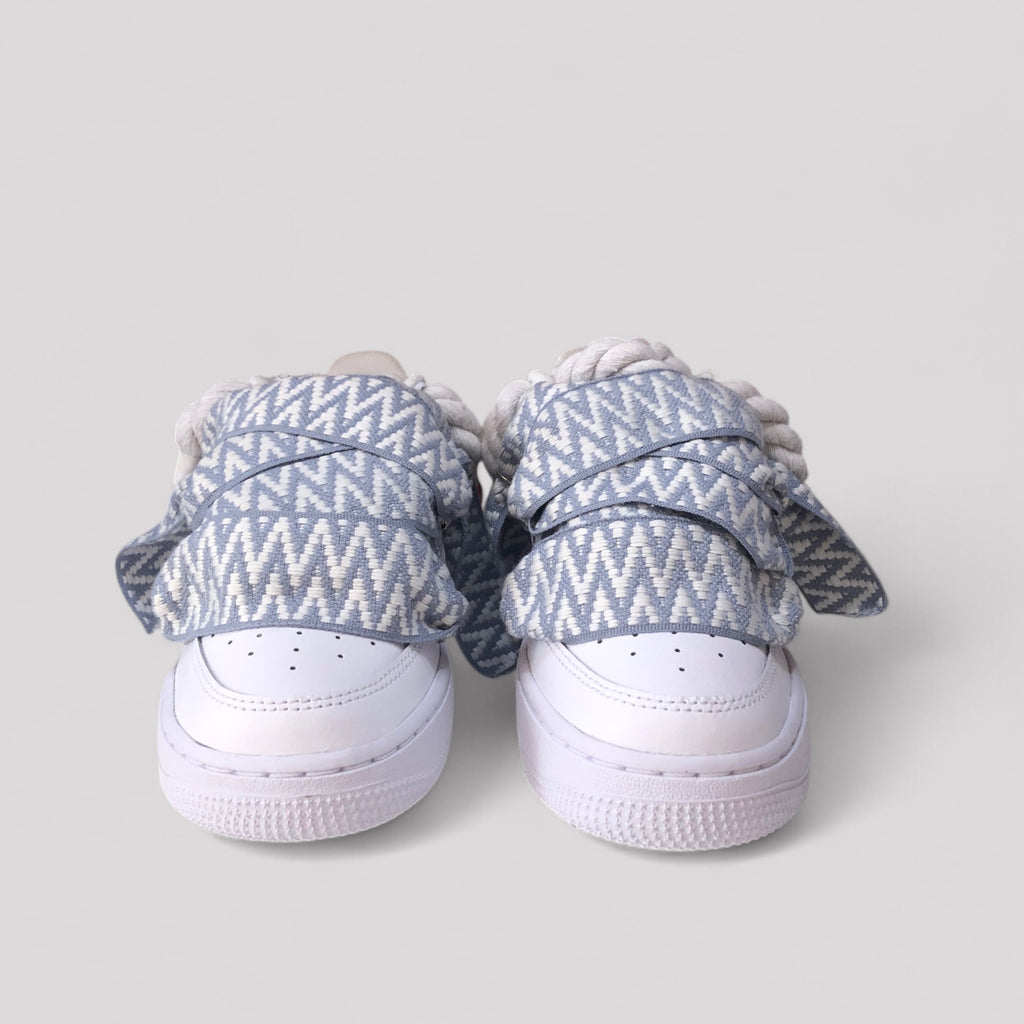 White sneakers with blue and white patterned shoelaces on a light gray background