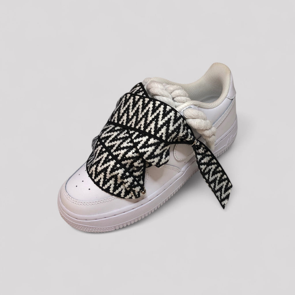 White sneaker with black and white patterned shoelace on a light gray background