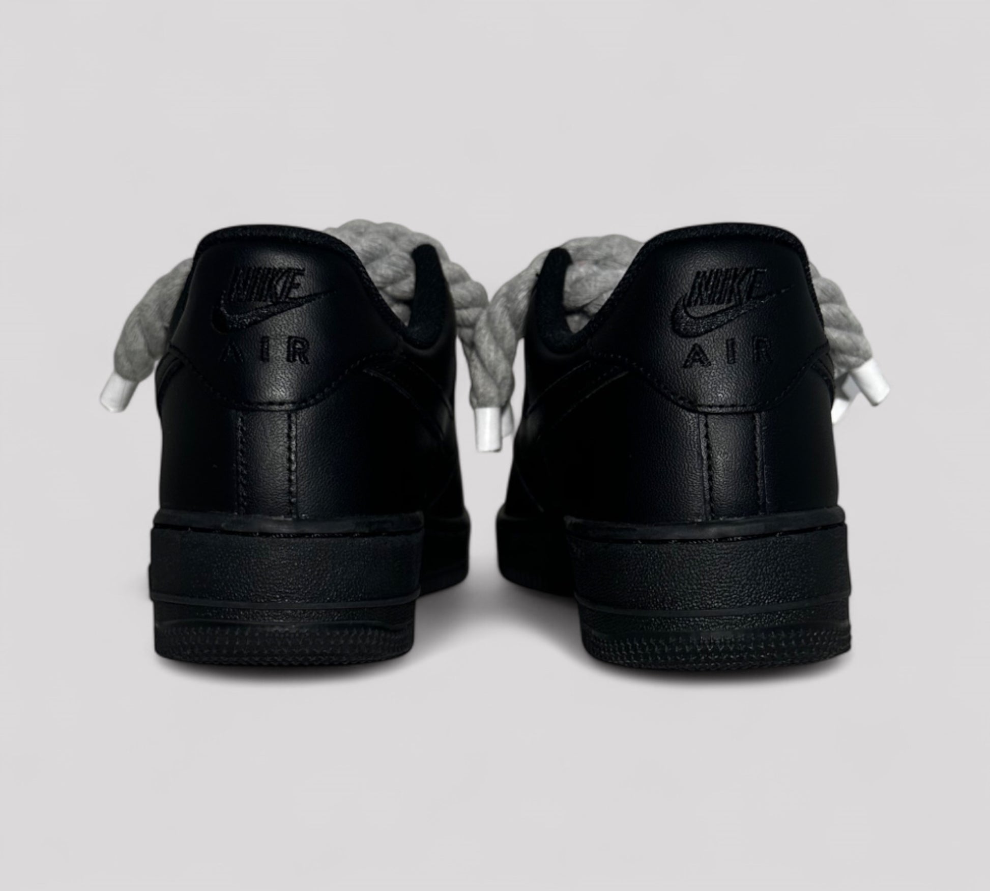 Black Nike Air Force sneakers shown from the back on a light gray background