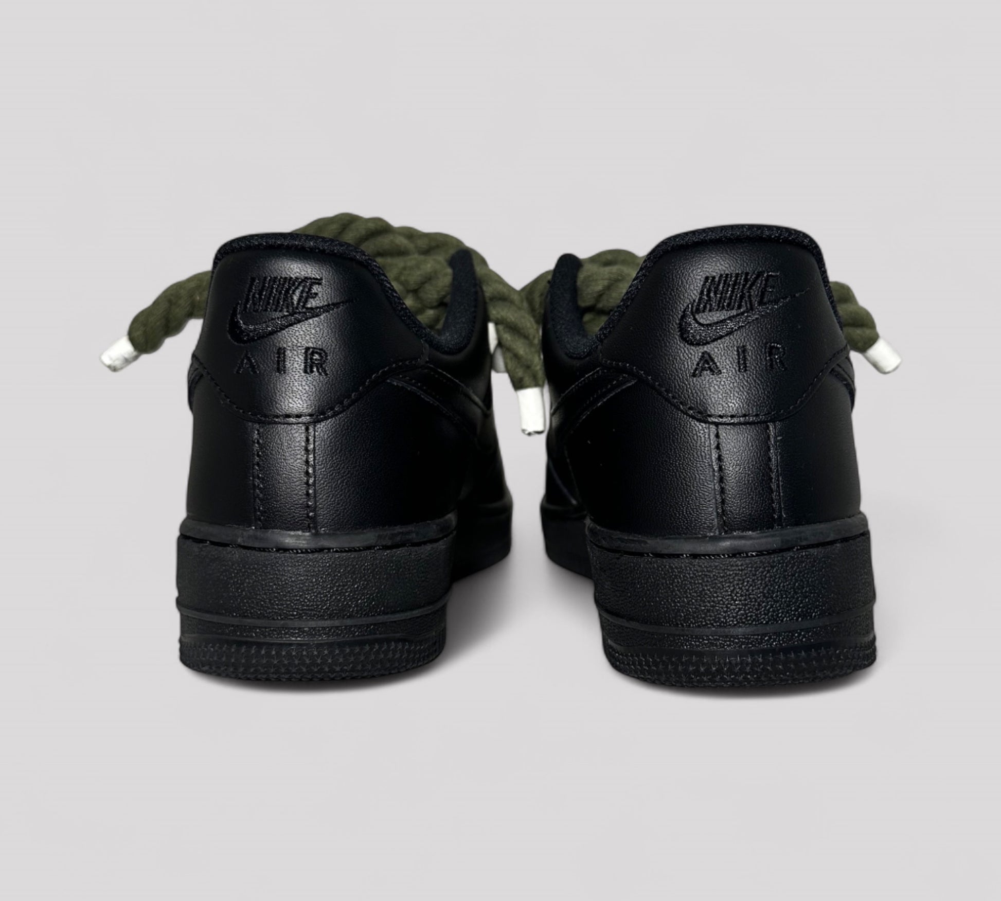 Black Nike Air shoes with khaki rope laces on a light gray background