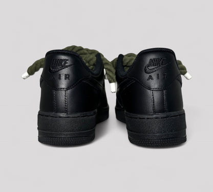 Black Nike Air shoes with khaki rope laces on a light gray background