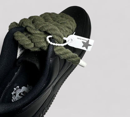 Black sneaker with green rope laces and a visible brand tag on a light gray background