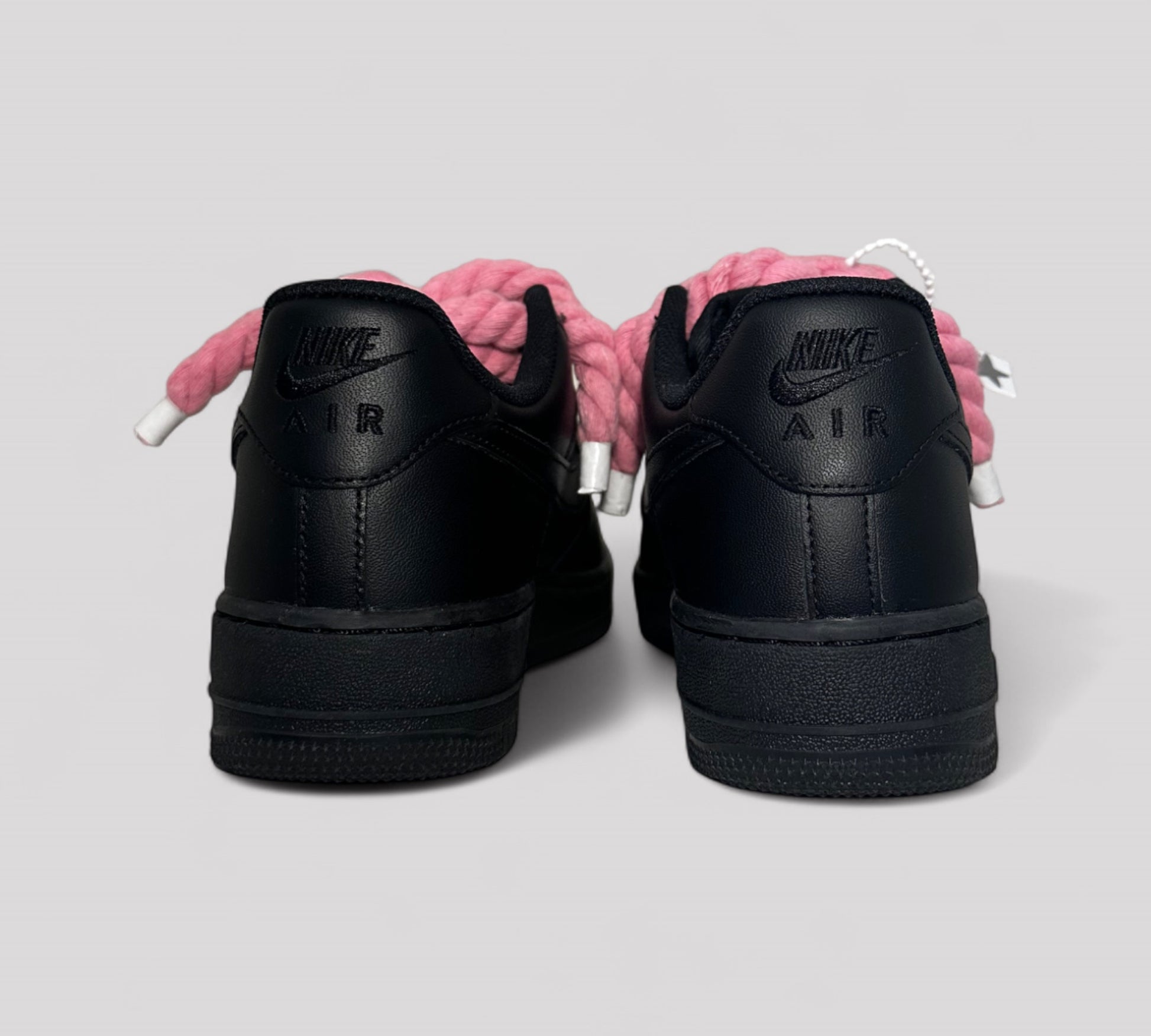 Black Nike Air Force sneakers with pink roep laces on a light gray background