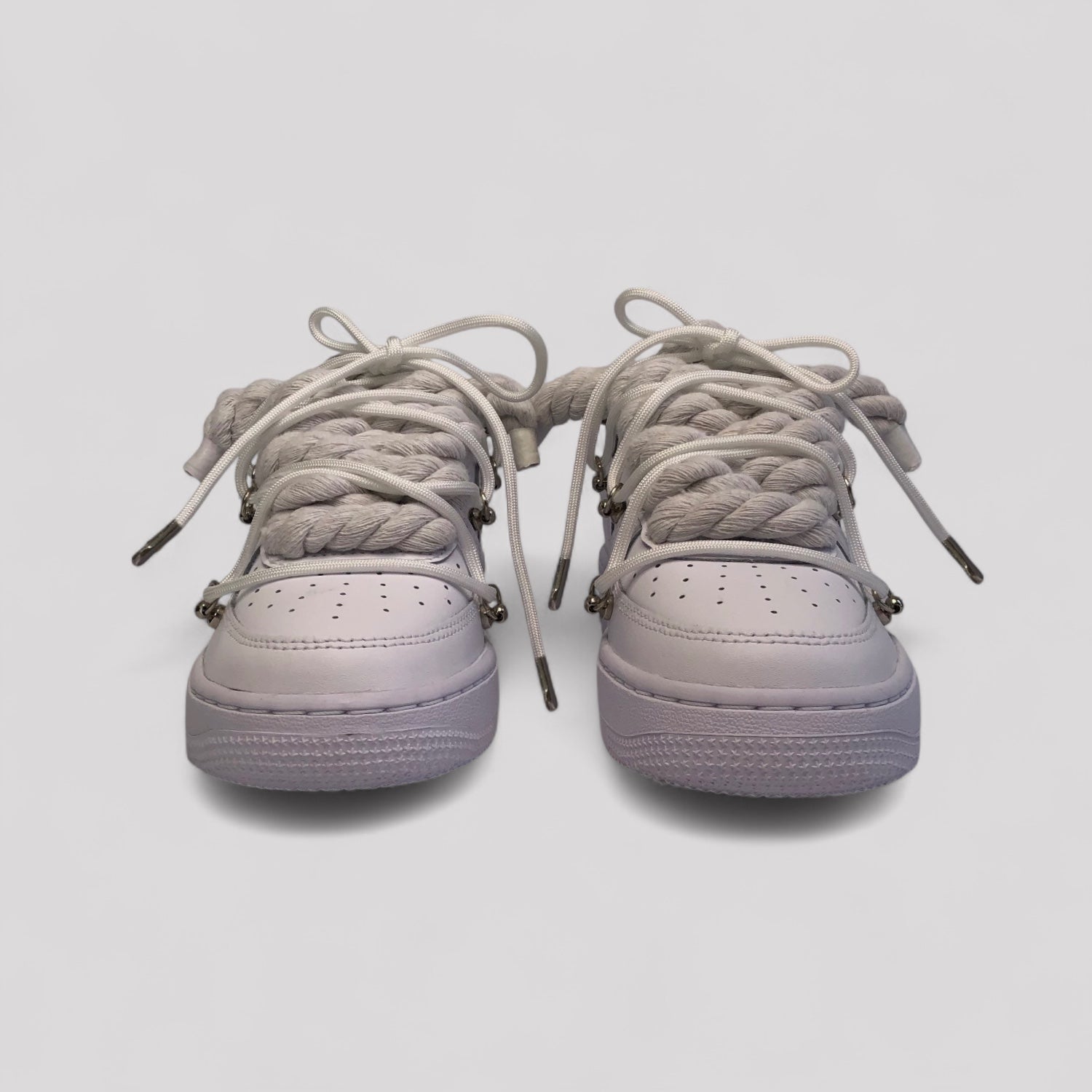 Pair of white nike air force 1 sneakers with braided laces on a shadow background